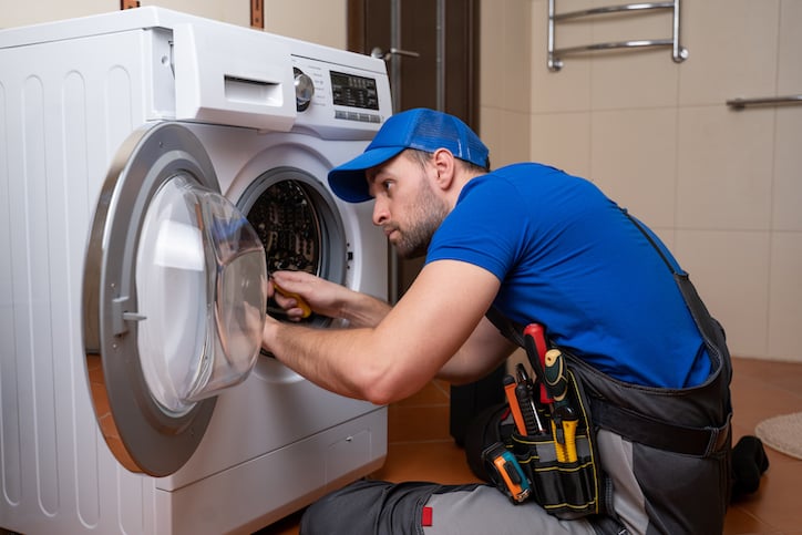 A facility maintenance worker performs equipment routine maintenance or repair services on a washing machine