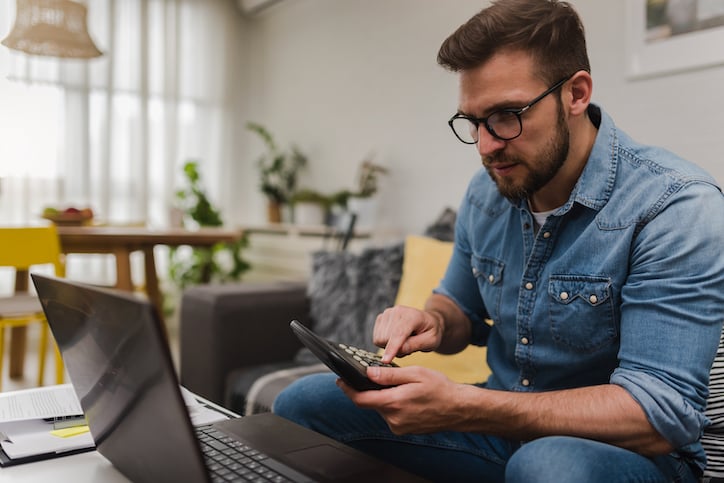 A man budgets in front of his laptop using facility management software that tracks KPIs related to preventative maintenance vs. regular maintenance and more